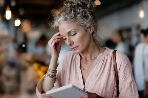 Nachdenkliche Frau prüft ihren Einkaufszettel in der Obst- und Gemüseabteilung eines Marktes.