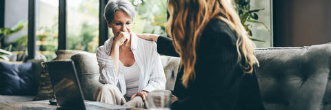 Gespräch zwischen zwei Generationen: Eine Seniorin im grünen Pullover spricht mit einer jungen Frau an einem Tisch.