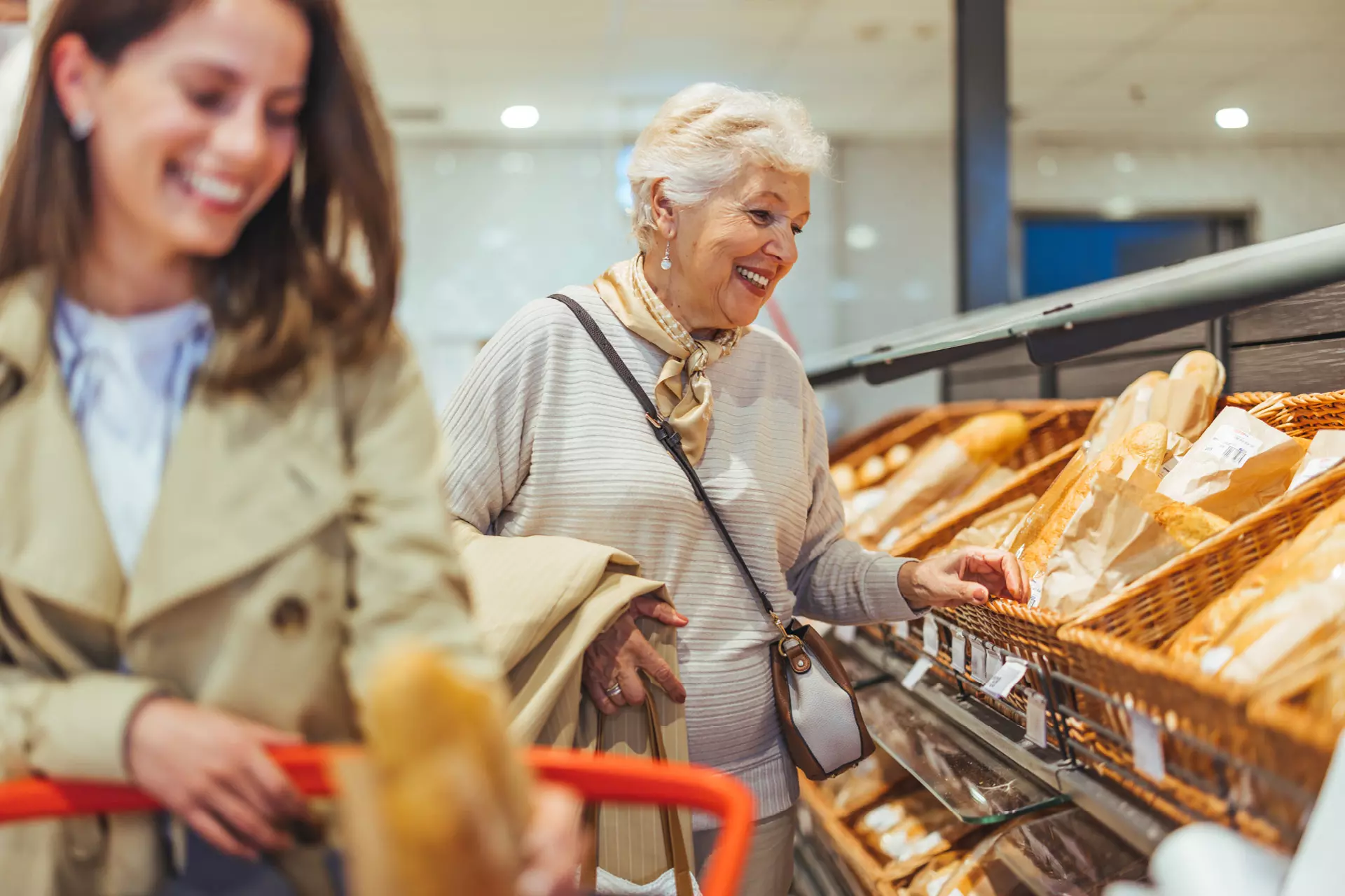 Zwei Frauen, eine jüngere und eine Seniorin, beim Bäcker, lächelnd